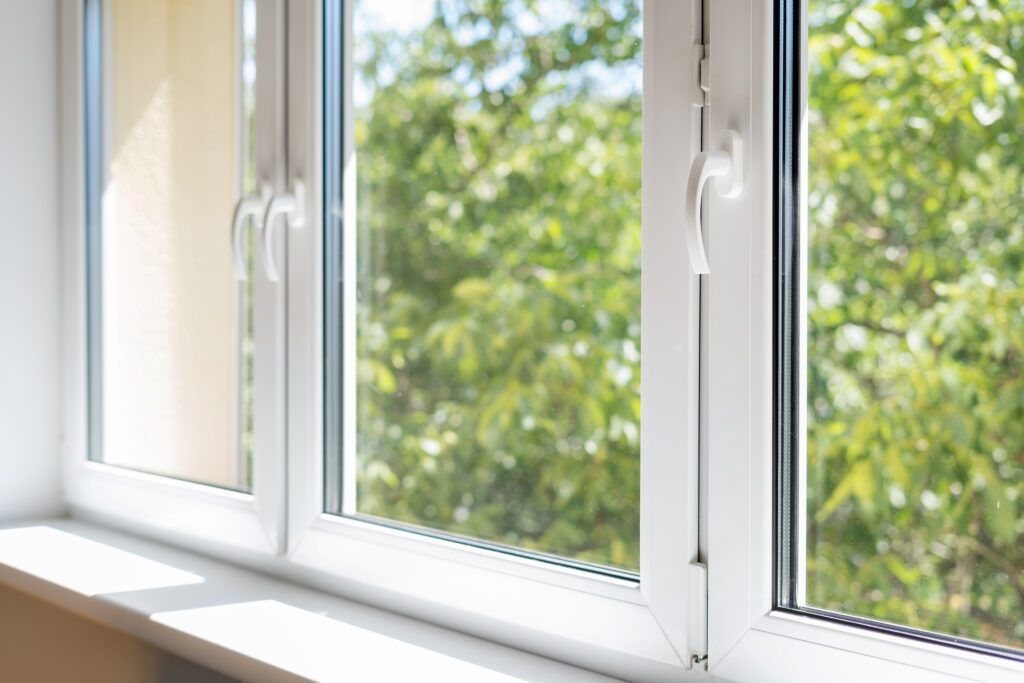 Ein modernes, weißes Fenster mit Blick auf grüne Bäume im Hintergrund. Das Fenster lässt viel Licht herein und zeigt klare, einfache Linien, die zu einem zeitgenössischen Hausdesign passen.