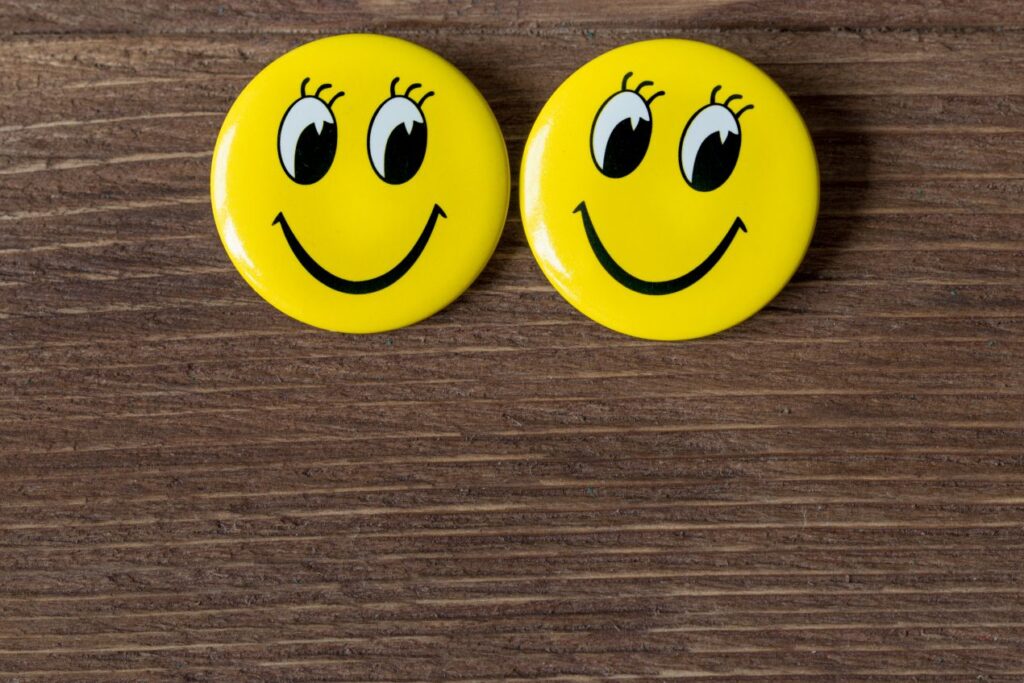 Zwei gelbe Smiley-Buttons auf Holztisch – Buttons bestellen mit persoenlichem Motiv oder fertige Designs fuer kreative Einsaetze nutzen