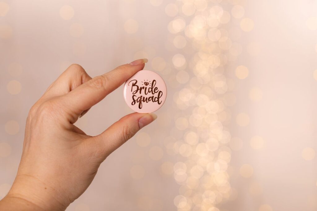Hand haelt rosa Anstecker mit Aufdruck „Bride Squad“ – ideal zum Buttons bestellen fuer Feiern, Teamaktionen oder Junggesellinnenabschiede