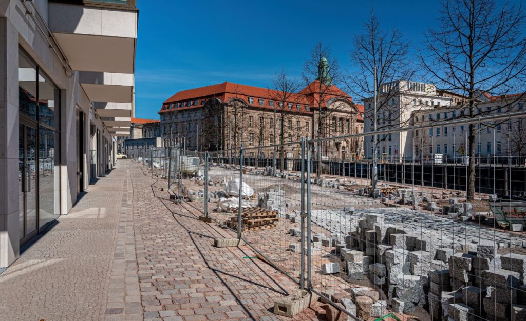Bauzaunbanner an Baustelle in historischer Innenstadt mit Pflastersteinen und Verwaltungsgebaeude